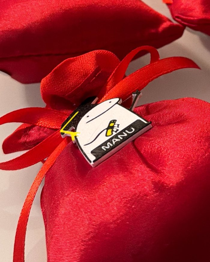 Primo piano della targhetta: tocco da laurea nero con fiocco giallo, faccia su fondo bianco e nome sulla fascia scura