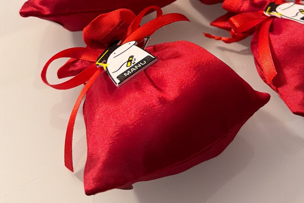 Sacchetto bomboniera in raso rosso con la targhetta stampata legata al nastro: tocco nero, fiocco giallo e nome