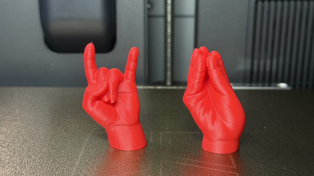 Due mani stampate in 3D in PLA rosso, le corna e la mano a borsa, appena uscite dalla stampante