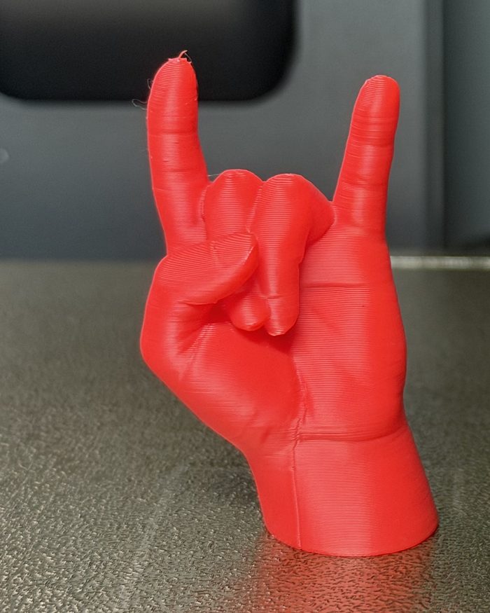 Primo piano della mano che fa le corna, in PLA rosso, con gli strati di stampa visibili sul polso