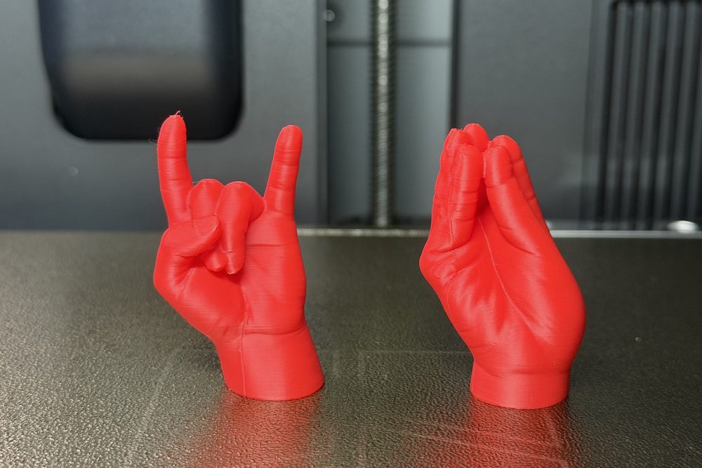 Due mani stampate in 3D in PLA rosso, le corna e la mano a borsa, appena uscite dalla stampante