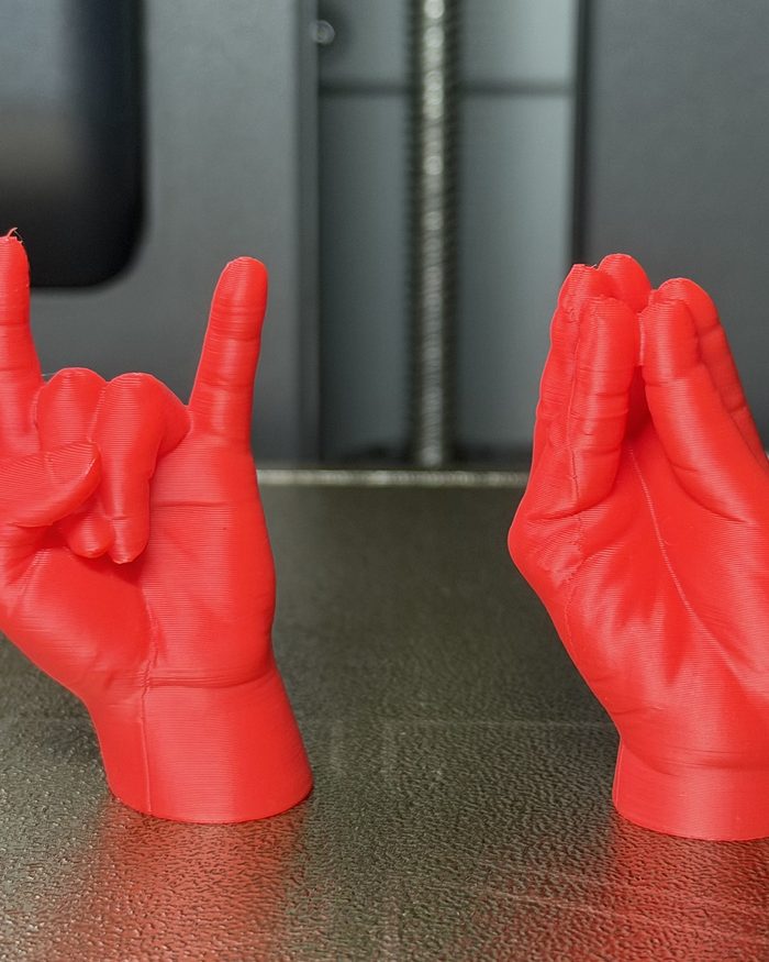 Due mani stampate in 3D in PLA rosso, le corna e la mano a borsa, appena uscite dalla stampante